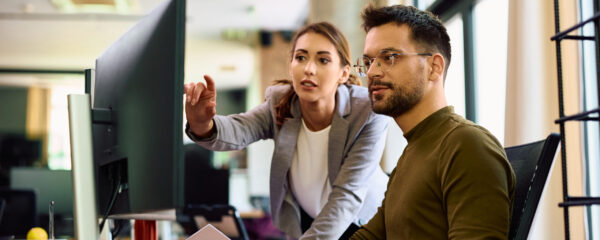 Young entrepreneur and his female coworker using desktop PC while working in the office.